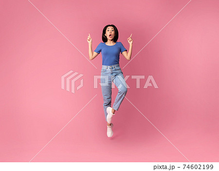 Surprised young asian woman jumping and pointing up Surprised young asian woman jumping and pointing up 74602199