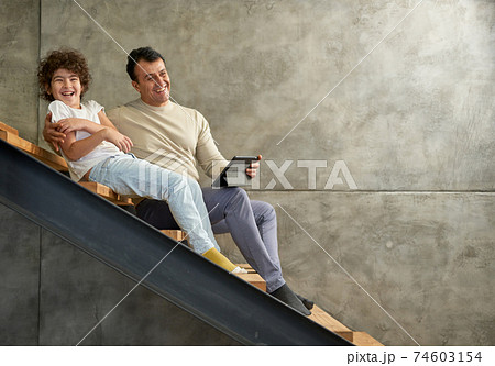 Full length shot of latin school boy smiling while sitting on the stairs with his father, using digital tablet pc while spending time together at home 74603154