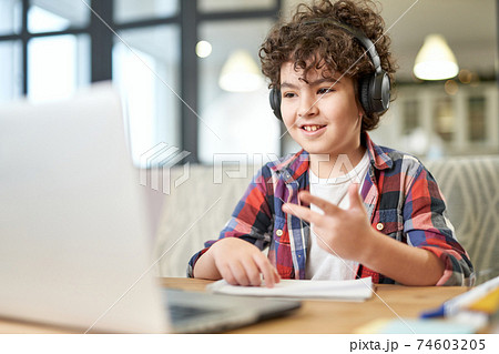 Get more knowledge. Happy latin american little boy wearing headphones, looking at the screen of a laptop while communicating with his teacher during online lesson at home Get more knowledge. Happy latin american little boy wearing headphones, looking at the screen of a laptop while communicating with his teacher during online lesson at home 74603205