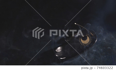 An incense stick on a palm rest is smoking on a black background 74603322