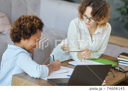 Learning excellence. Joyful mixed race teen schoolgirl writing during a lesson with her female teacher at home 74606145