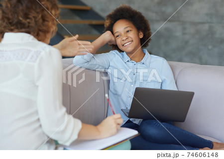 Mixed race teen girl smiling at her female teacher, using laptop for studying while having a lesson, sitting on the sofa at home Mixed race teen girl smiling at her female teacher, using laptop for studying while having a lesson, sitting on the sofa at home 74606148