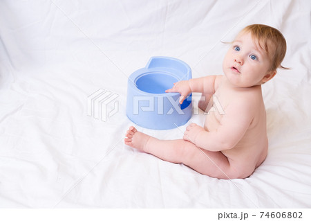 Cute Caucasian toddler sits near a blue nursery pot on a white Cute Caucasian toddler sits near a blue nursery pot on a white 74606802