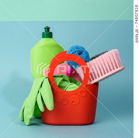 basket with washing sponges, rubber protective gloves, brushes and cleaning agent in a green plastic bottle on a blue background 74607816