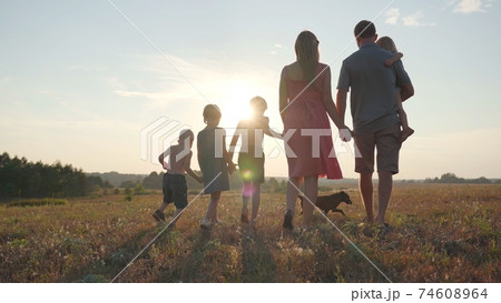 A friendly large family walks across the field at sunset with dog. 74608964