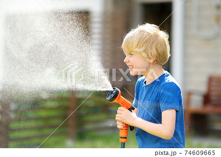 Funny little boy watering lawn and playing with garden hose with sprinkler in sunny backyard. Funny little boy watering lawn and playing with garden hose with sprinkler in sunny backyard. 74609665