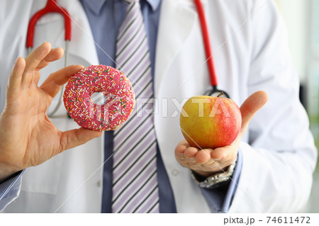 Doctor in office holding in hand pink doughnut vs red apple Doctor in office holding in hand pink doughnut vs red apple 74611472