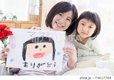 母の日カーネーションと似顔絵を貰ったママと女の子のポートレートの写真素材 母の日カーネーションと似顔絵を貰ったママと女の子のポートレートの写真素材
