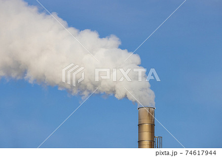 工場の銀色の煙突が吐き出す白い煙の写真素材