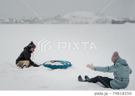 Man pulling snow tube with girlfriend. Young happy couple walking in winter day 74618350