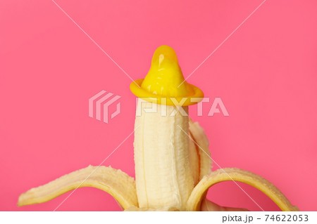 Banana with condom on pink background, close up Banana with condom on pink background, close up 74622053