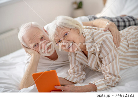 Grey-haired woman showing something on a tablet to her husband Grey-haired woman showing something on a tablet to her husband 74622332