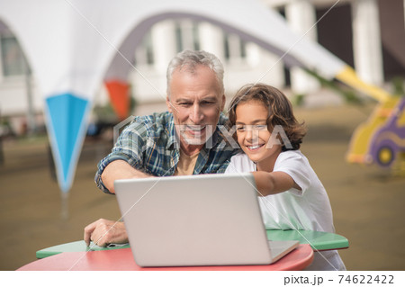 Son and dad sitting together with a laptop and looking contented 74622422
