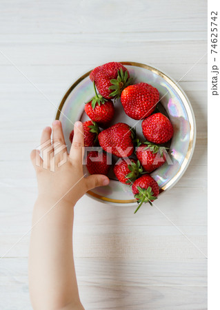 Hand of a child with a strawberry on a rustic background, a plate of strawberries. Hand of a child with a strawberry on a rustic background, a plate of strawberries. 74625742