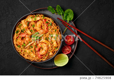 Mie Goreng in black bowl on dark slate table top. Indonesian cuisine prawn noodles vegetables dish Mie Goreng in black bowl on dark slate table top. Indonesian cuisine prawn noodles vegetables dish 74625908