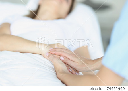 On bed lies a sick doctor sitting next to him and sympathetically holds hand On bed lies a sick doctor sitting next to him and sympathetically holds hand 74625960