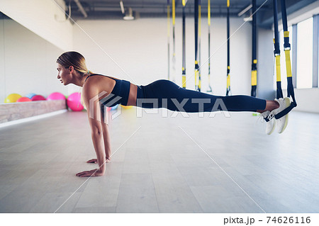 Beautiful young woman training with suspension trainer sling or 74626116