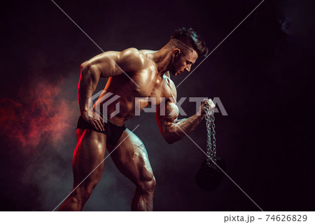 Athletic man flexing muscles in studio on dark background with smoke. Strong bodybuilder with perfect abs 74626829