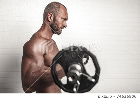 Bodybuilder doing exercises for biceps with a barbell against br Bodybuilder doing exercises for biceps with a barbell against br 74626906