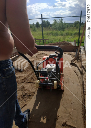 The worker controls the vibrating plate at the construction site, heavy manual construction equipment, pressing and compaction of sand. 74627979