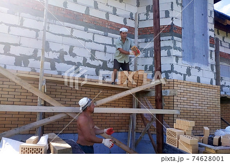 A worker throws bricks at another worker, construction work in a private area, wooden scaffolding near the walls. A worker throws bricks at another worker, construction work in a private area, wooden scaffolding near the walls. 74628001