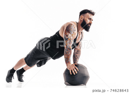 Muscular tattooed bearded male exercising fitness weights Medicine Ball push ups exercises in studio isolated on white background Muscular tattooed bearded male exercising fitness weights Medicine Ball push ups exercises in studio isolated on white background 74628643