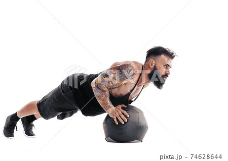Muscular tattooed bearded male exercising fitness weights Medicine Ball push ups exercises in studio isolated on white background 74628644