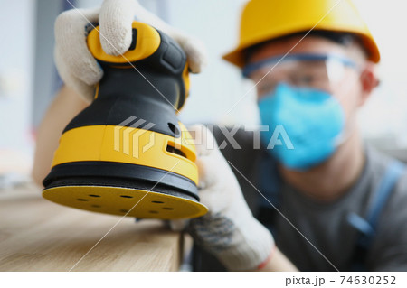 Master builder in protective mask is holding disc sander Master builder in protective mask is holding disc sander 74630252