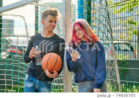 Couple on sports basketball court talking, standing with ball and bottle of water Couple on sports basketball court talking, standing with ball and bottle of water 74630705
