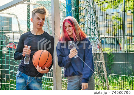 Couple on sports basketball court talking, standing with ball and bottle of water Couple on sports basketball court talking, standing with ball and bottle of water 74630706