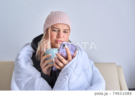Cold autumn winter season, teenage girl sitting under blanket using smartphone 74631089