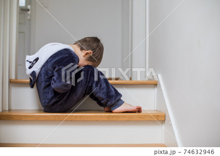 the unhappy child is sitting on the stairs with his head down 74632946