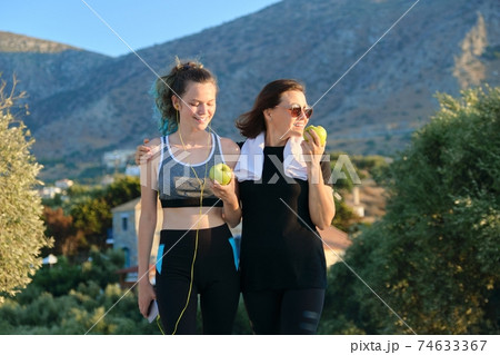 Mother and teenage daughter eating apples after jogging on sunset mountain road Mother and teenage daughter eating apples after jogging on sunset mountain road 74633367