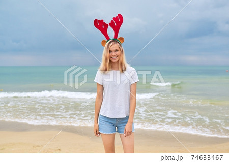 Beautiful young woman walking on the beach in Christmas deer ears Beautiful young woman walking on the beach in Christmas deer ears 74633467