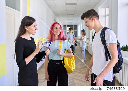 Group of teenage students talking to a female teacher in school corridor Group of teenage students talking to a female teacher in school corridor 74633509
