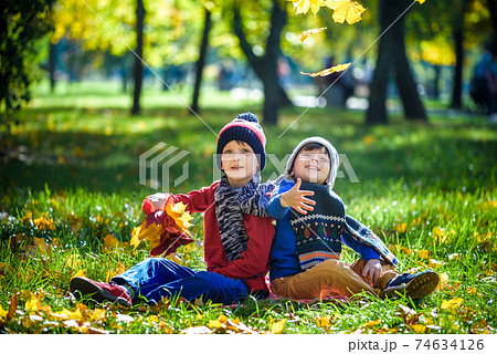 Happy children playing in beautiful autumn park on warm sunny fall day. Kids play with golden maple leaves. 74634126