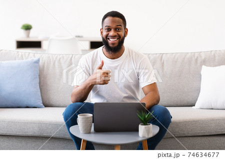 Black Man At Laptop Gesturing Thumbs-Up To Camera At Home Black Man At Laptop Gesturing Thumbs-Up To Camera At Home 74634677