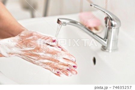 Young woman washing her hands under water tap faucet with soap. Detail on suds covered skin. Personal hygiene concept - coronavirus covid 19 outbreak prevention Young woman washing her hands under water tap faucet with soap. Detail on suds covered skin. Personal hygiene concept - coronavirus covid 19 outbreak prevention 74635257
