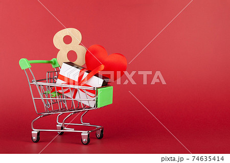 Red heart, gift box with red ribbon inside mini grocery cart on colored background Red heart, gift box with red ribbon inside mini grocery cart on colored background 74635414