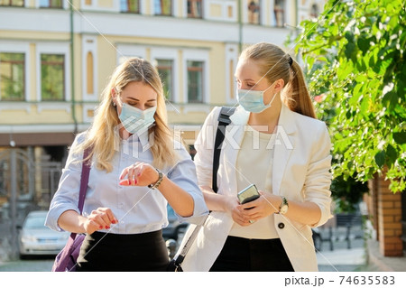 Office workers two women walking, wearing medical protective masks Office workers two women walking, wearing medical protective masks 74635583