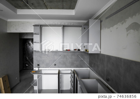 Custom kitchen cabinets installation without a furniture facades mdf. Gray modular kitchen from chipboard material on a various stages of installation in kitchen with a grey tile on floor and walls. Custom kitchen cabinets installation without a furniture facades mdf. Gray modular kitchen from chipboard material on a various stages of installation in kitchen with a grey tile on floor and walls. 74636856