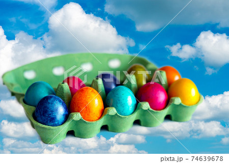 Colorful eggs in a open carton box on blue sky background.eggs flies over whites clouds. Colorful eggs in a open carton box on blue sky background.eggs flies over whites clouds. 74639678