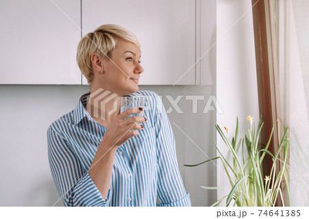 Woman holding glass with water in kitchen in morning Woman holding glass with water in kitchen in morning 74641385