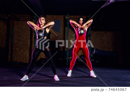 Two Attractive fit women athlete performing a kettle-bell swing 74645067