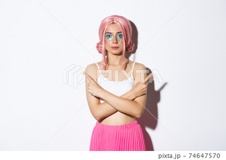 Indecisive young woman in pink wig and halloween costume, pointing sideways at two choices, showing variants, standing over white background 74647570