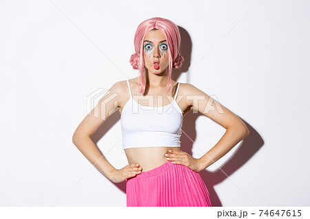 Image of silly party girl with pink wig and bright makeup, celebrating halloween, looking surprised, standing over white background 74647615