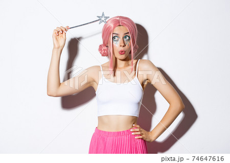 Image of silly attractive girl in pink wig, dressing as fairy for halloween party, hoding magic wand, standing over white background 74647616
