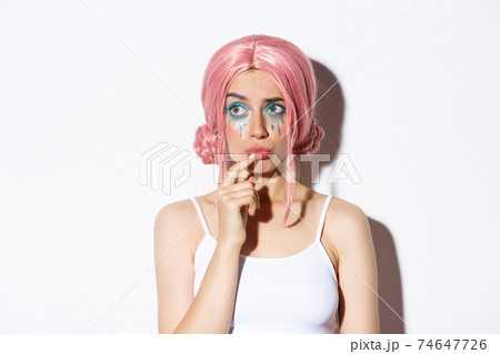 Close-up of concerned cute girl in pink party wig, looking left and thinking, standing over white background in halloween costume 74647726