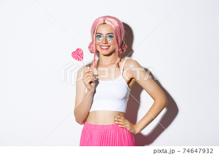 Beautiful smiling girl in pink wig, holding heart-shaped candy, trick or treating in fairy costume on halloween, standing over white background 74647932