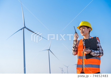 female engineer using walkie talkie to checking system against wind turbine farm female engineer using walkie talkie to checking system against wind turbine farm 74652483
